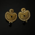 A pair of ornate gold-toned Indian jhumka earrings decorated with clear kundan stones and black bead accents, displayed on a reflective black surface. The brand logo 'SAHELI MY BESTFRIEND' is visible in the top left corner.
