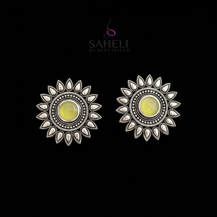 Silver sun-shaped earrings with yellow centers on a gray background, featuring the brand 'Saheli'.