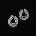 A pair of silver-toned teardrop-shaped earrings with intricate filigree cutouts and clear stones, displayed on a dark reflective surface.