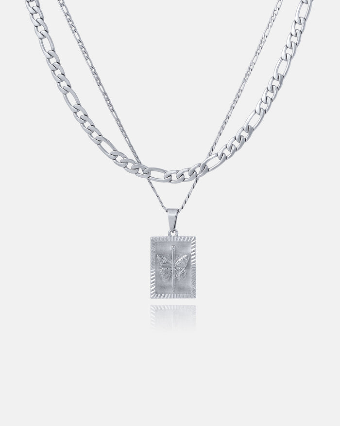 The Figaro Set (Custom Pendant Choice) features two layered silver chains: a flat curb chain and a thinner Figaro chain with a rectangular pendant displaying a raised butterfly design, shown on a plain white background.