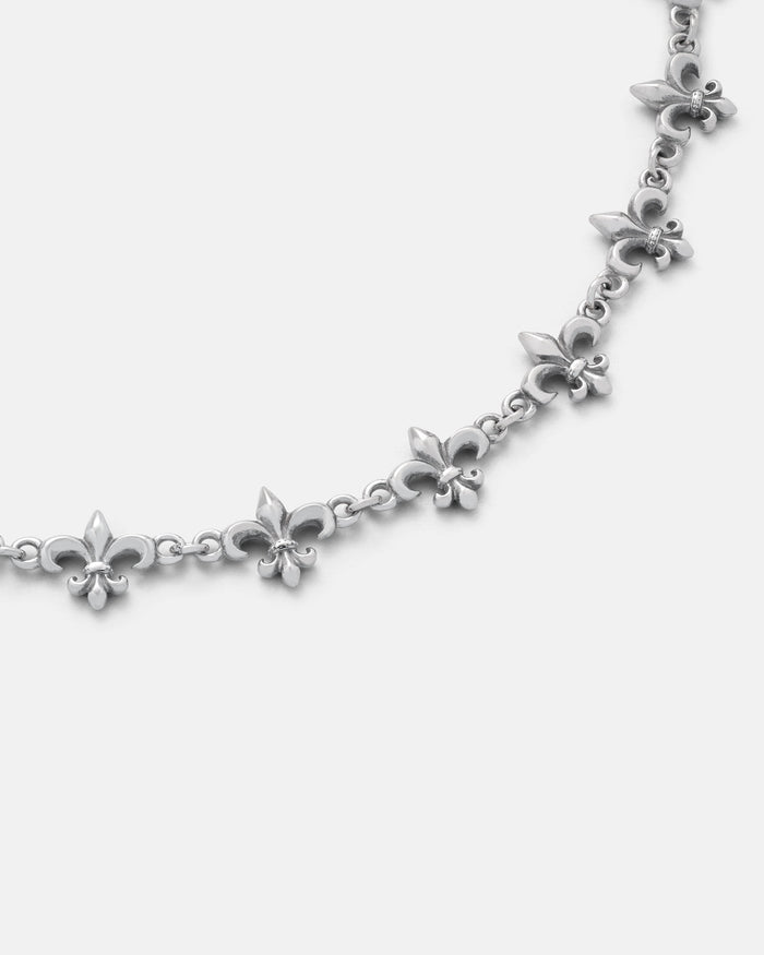 The "Fleur De Lis" 10mm Chain by Statement Collective showcases a repeating pattern of small and large fleur-de-lis charms linked together, displayed on a plain white background.