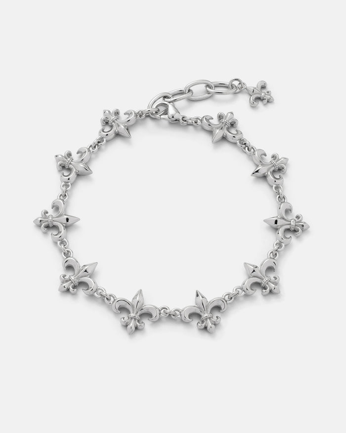 The "Fleur De Lis" 15mm Bracelet by Statement Collective showcases a silver design with alternating fleur-de-lis and pointed spike charms, finished with a lobster clasp and a small dangling fleur-de-lis charm at the end.