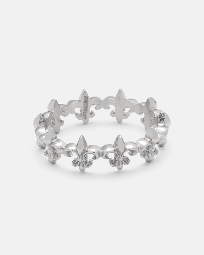 The “Fleur De Lis” Ring by Statement Collective is crafted in silver and features a repeating fleur-de-lis pattern around the band. Displayed on a white background, this stackable ring is perfect for creating a unique, layered look.