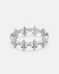The “Fleur De Lis” Ring by Statement Collective is crafted in silver and features a repeating fleur-de-lis pattern around the band. Displayed on a white background, this stackable ring is perfect for creating a unique, layered look.