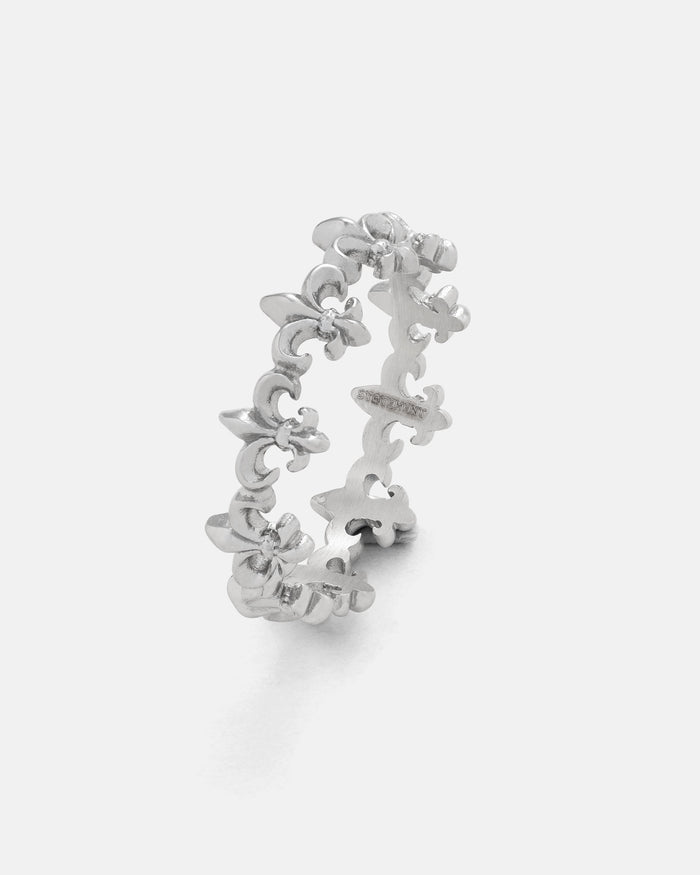 The “Fleur De Lis” Ring by Statement Collective showcases a repeating pattern of upright fleur-de-lis shapes in silver, displayed against a plain white background—ideal for stacking and versatile styling.