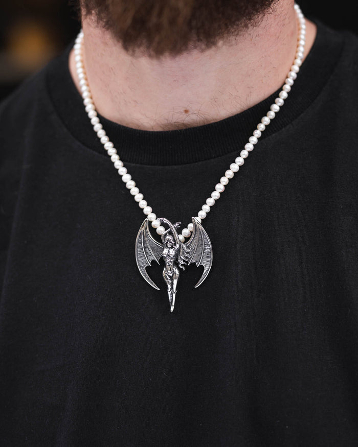 Someone wears the Freshwater Pearl Necklace With Custom Pendant Choice, featuring a silver winged humanoid pendant, over a plain black shirt.