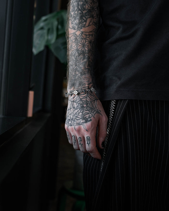 Person with tattooed arm wearing a steel bracelet of dice links and crosses by statement collective in a dark room