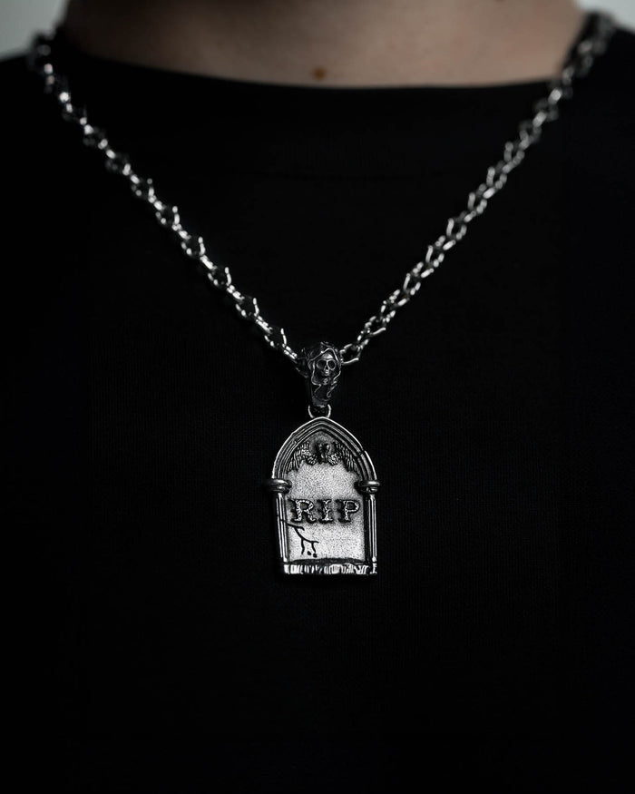 The Gravestone Pendant is a silver necklace with a tombstone-shaped charm engraved with RIP and Roman numerals. Wear it over a black shirt for a bold, macabre statement.