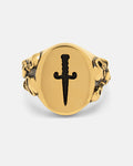 The Graveyard Signet Ring (Gold) by Statement Collective features a bold flat oval face engraved with a black dagger, perfectly capturing the essence of gothic jewelry. Intricately sculpted lion heads grace both sides of the 18k gold band, lending an air of mystery and striking sophistication to this unique piece.