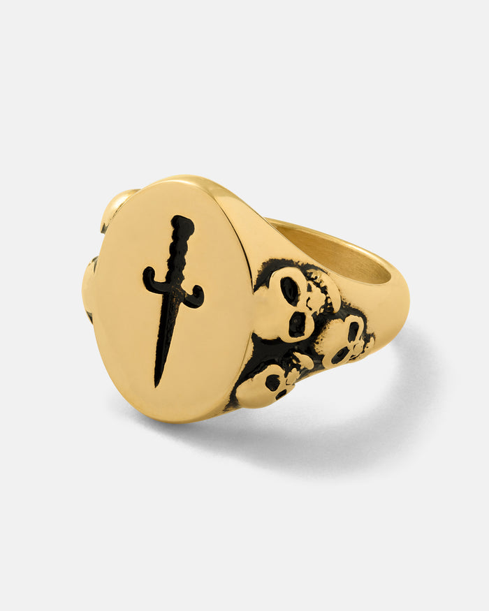 The Graveyard Signet Ring (Gold) by Statement Collective is a bold piece of gothic jewelry, crafted in 18k gold with a flat circular face engraved with a dagger and small sculpted skull details along the band—perfect for those who appreciate dark elegance.