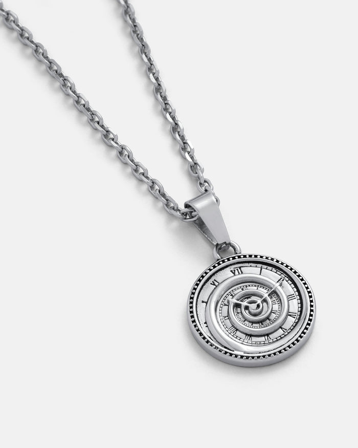 The Infinite Clock Pendant Necklace is a silver chain featuring a spiral clock pendant with Roman numerals in a surreal design, creating a striking, unique look against any light background.