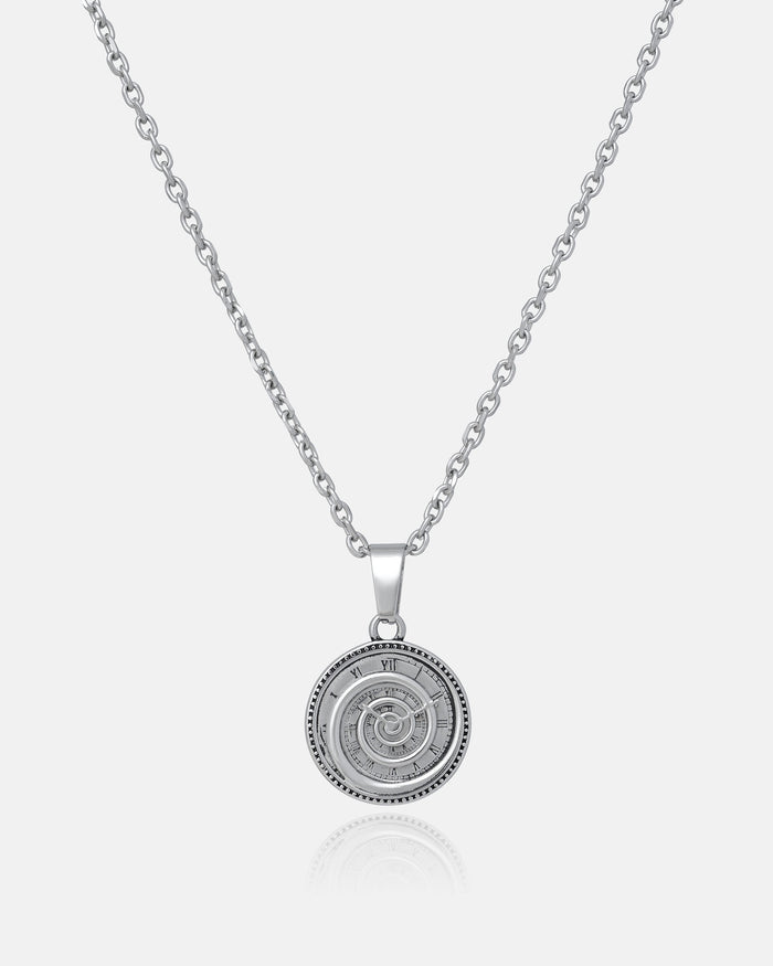 The Infinite Clock Pendant Necklace features a silver chain and a round clock pendant with an intricate spiral design and Roman numerals, showcased against a plain white background.