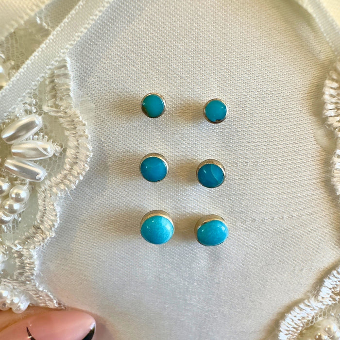 Wildflower Artisans turquoise stud earrings in small, medium, and large sizes on a white lace background.