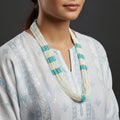 Long necklace with white beads and blue accents on a dark background