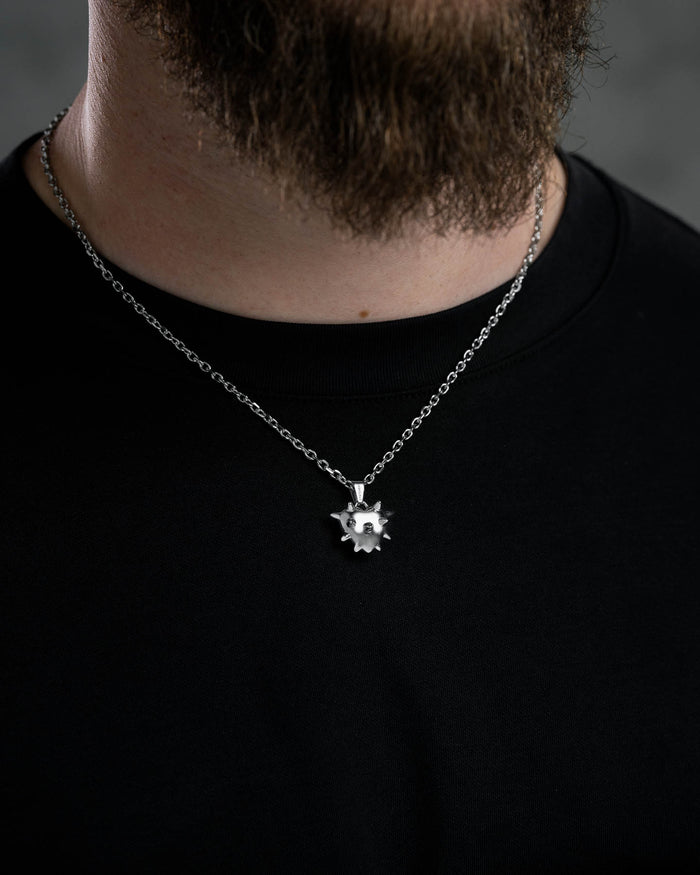 A close-up of a person in a black shirt wearing the Mini "Love Hurts" Spiked Heart Pendant necklace. The dark, blurred background highlights the bold, stainless steel statement jewelry.