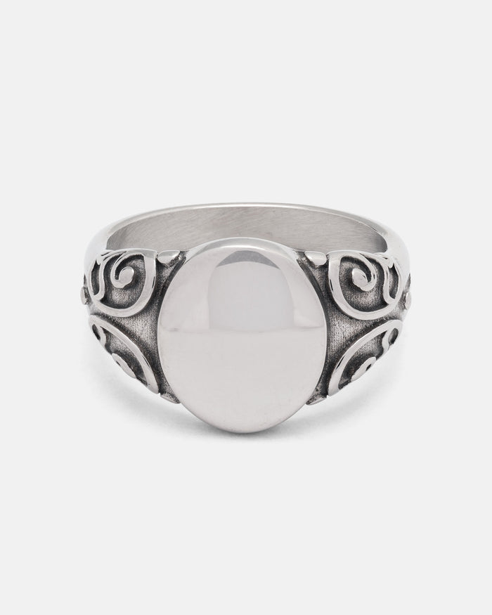 The Mini Oval Scroll Signet Ring by Statement Collective features a polished silver centerpiece and an ornate traditional scroll pattern swirling along the band, displayed on a plain white background.