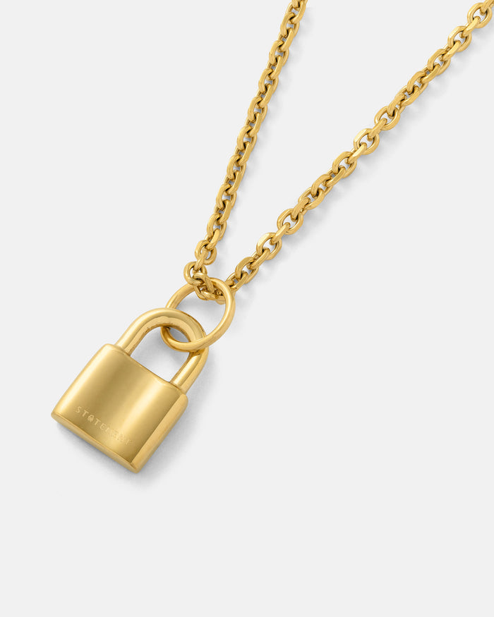 The Mini Padlock Pendant (Gold) is an 18k gold, hypoallergenic necklace featuring a shiny padlock charm displayed on a simple light background.