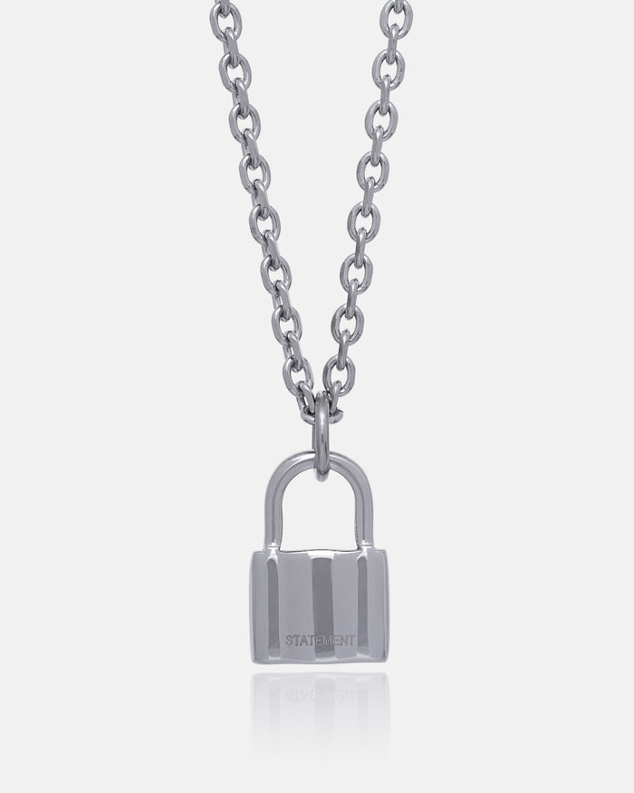 The Mini Padlock Pendant is a silver necklace with a 2mm chain, featuring a padlock-shaped pendant engraved with "STATEMENT," shown on a plain white background.