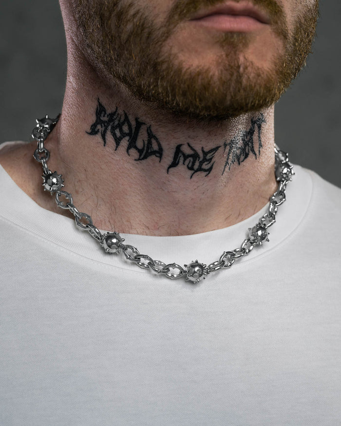 A bearded man in a white shirt wears a chunky "Morning Star" Cathedral Chain necklace. He has “HOLD MY ART” tattooed in bold, stylized black letters on his neck.