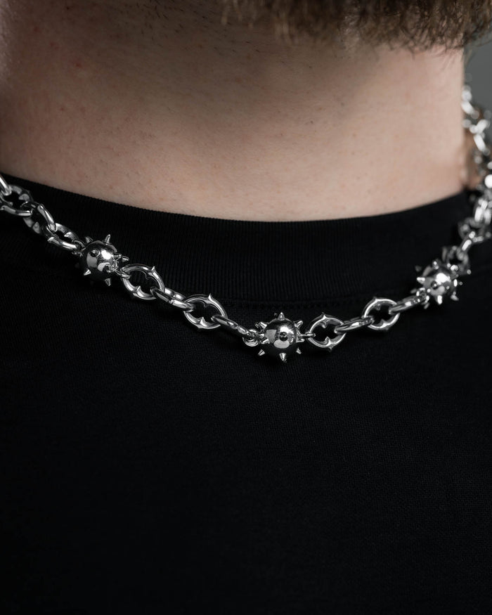 A close-up of a person wearing the "Morning Star" Cathedral Chain, a stainless steel necklace featuring spiked metal ball details, paired with a plain black shirt.