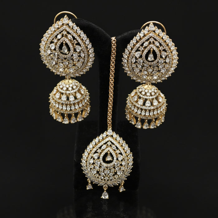 Ornate gold earrings with intricate designs on a dark stand, branded 'Saheli'.