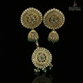 Ornate gold earrings with green stones on a dark stand, branded 'Saheli'.