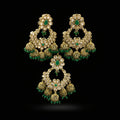 Gold and green earrings on a black stand with 'Saheli' branding.
