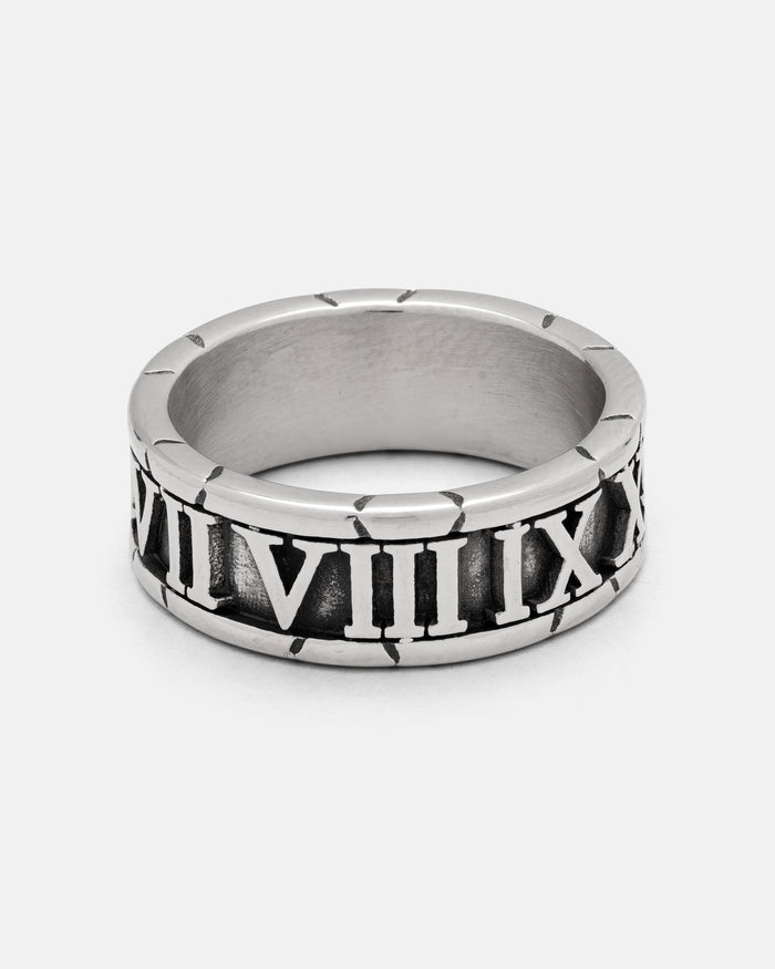 The Numerals Ring by Statement Collective is a striking accessory crafted from polished stainless steel, featuring bold black engraved Roman numerals from VII to XII elegantly wrapped around the band. Perfect as a statement piece or stacking band, this silver ring is beautifully displayed on a crisp white background.