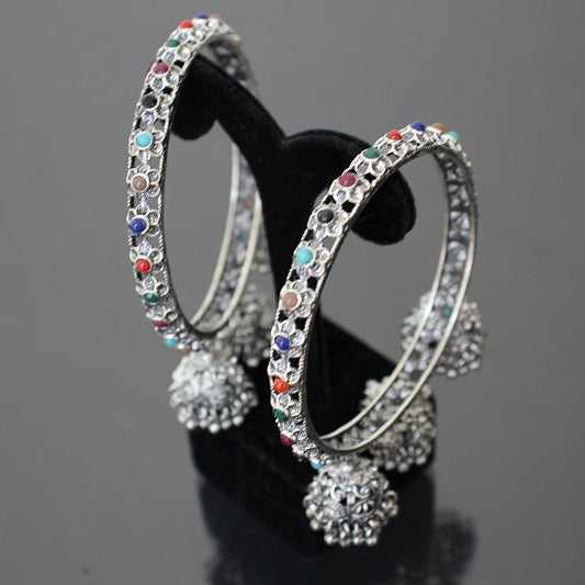 Decorative hoop earrings with colorful gemstones on a black stand against a dark background
