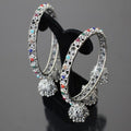 Decorative hoop earrings with colorful gemstones on a black stand against a dark background