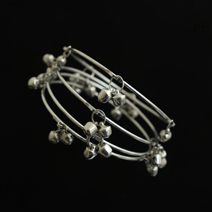 Set of silver anklets with small bells on a dark gray stand, brand 'Saheli' visible.