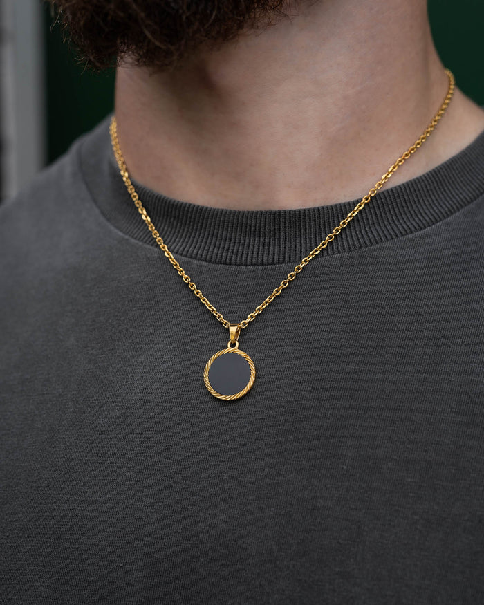 A person wears a plain dark gray shirt and a gold chain featuring the Onyx Medallion Pendant (Gold). The focus is on the striking necklace and medallion, with only the lower part of their face visible.