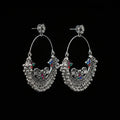 Pair of silver hoop earrings with colorful gemstones on a gray stand against a dark background