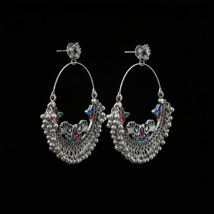 Pair of silver hoop earrings with colorful gemstones on a gray stand against a dark background