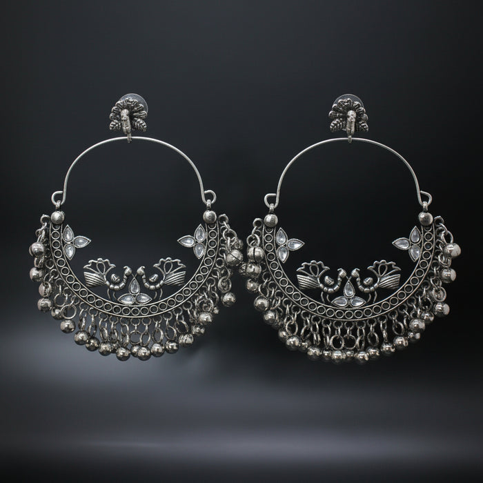 Pair of silver hoop earrings with intricate designs on a gray stand against a dark background