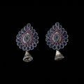 Pair of ornate earrings with purple and blue stones on a dark background, branded 'SAHELI'.
