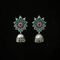 Ornate silver earrings with green and red stones on a black background