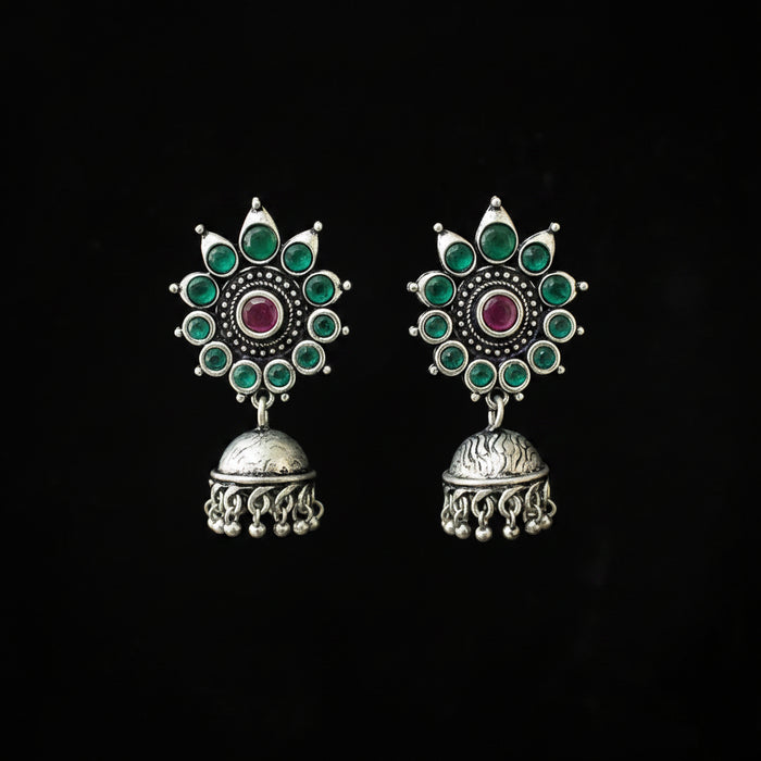 Ornate silver earrings with green and red stones on a black background