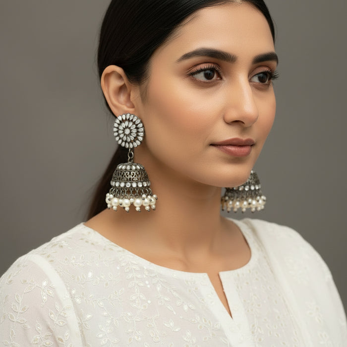 Silver and pearl earrings on a gray stand with 'Saheli' branding.