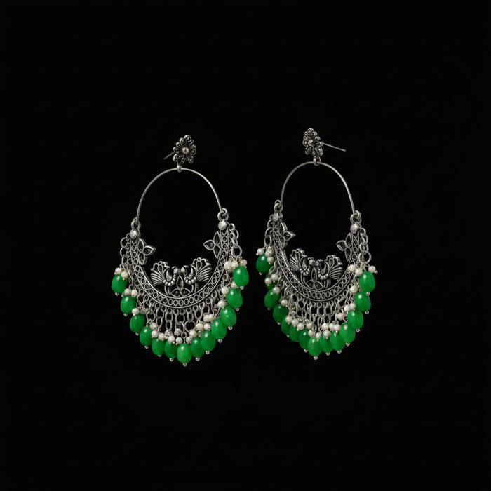 Ornate hoop earrings with green beads on a dark background