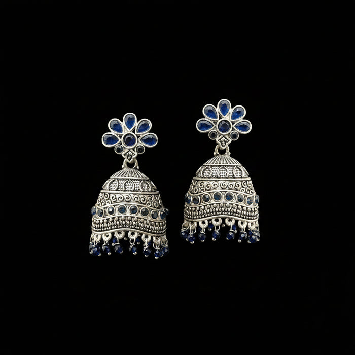 A pair of silver-toned Indian jhumka earrings with blue stone accents, displayed on a gray velvet jewelry stand against a light gray background.