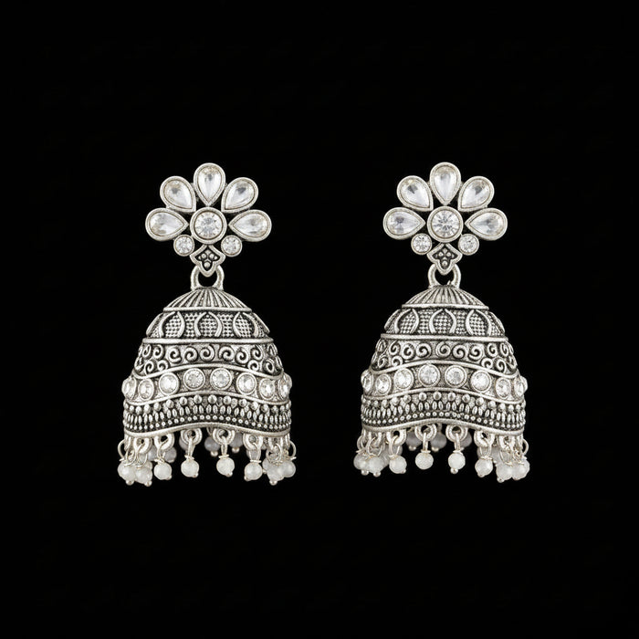 A pair of silver-toned Indian jhumka earrings with blue stone accents, displayed on a gray velvet jewelry stand against a light gray background.