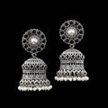 Pair of silver jhumka earrings with black stones and pearl accents on a gray stand.