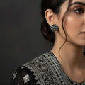 A pair of silver-toned circular earrings with black circular details, displayed on a dark reflective surface.