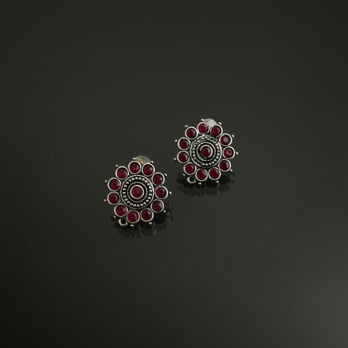 A pair of silver-toned Indian-style stud earrings with red stones, displayed on a dark reflective surface with the brand logo 'SAHELI BY BEST FRIEND' above them.