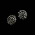 A pair of round silver-toned earrings with intricate floral and geometric filigree patterns, displayed on a dark reflective surface.