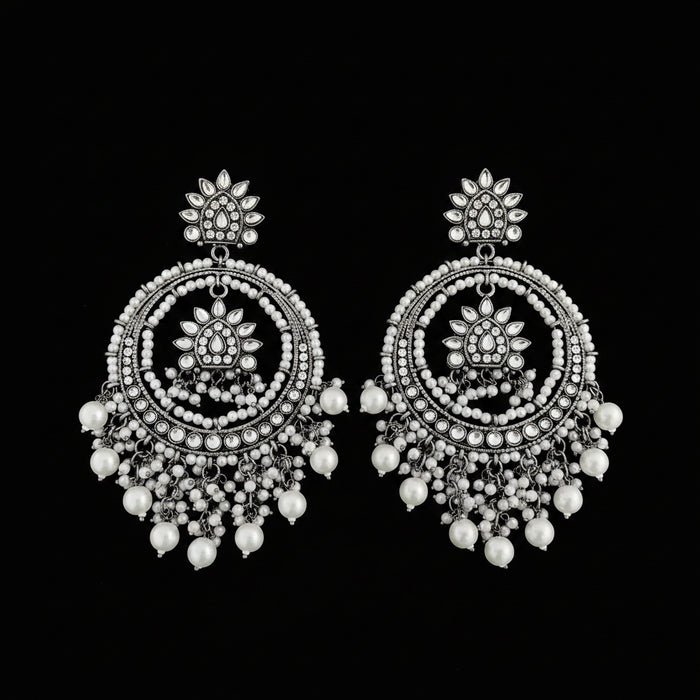 A pair of ornate silver-toned dangle earrings with intricate circular beadwork, floral motifs, and dangling pearl-like beads, displayed on a dark reflective surface.