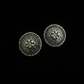 A pair of round silver-toned metal buttons with intricate floral and geometric filigree detailing, displayed on a dark reflective surface.