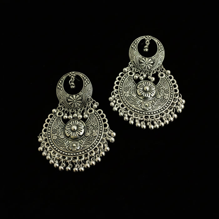 A pair of ornate silver-toned Indian jhumka earrings with intricate filigree work and dangling bead chains, displayed on a dark reflective surface.