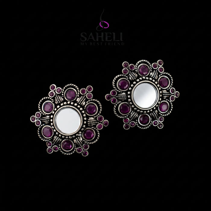 Ornate silver and purple earrings on a gray background with 'Saheli' branding.